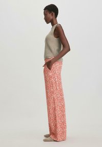 Lichtgroene gebreide tanktop gecombineerd met loszittende, bloemenpatroon broek in tinten rood en crèmekleur, met zijzakken.