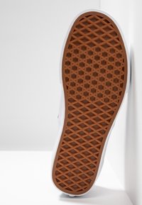 Semelle de chaussure avec motif gaufré en caoutchouc marron, semelle intermédiaire blanche, présentée debout sur fond blanc.