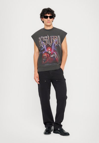 Débardeur gris graphique sans manches avec le logo du groupe, présentant une œuvre d'art colorée et audacieuse ; associé à un pantalon cargo noir et des chaussures noires.