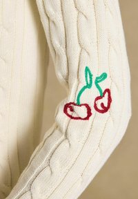 Kreemikas soonikkoes kampsunisärk varrukas, küünarvarre piirkonnas punase ja rohelise tikandiga kirsside kujutis.