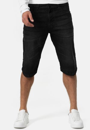 Sorte denimshorts med en tilspidset pasform, opkrogede kanter og fem-lomme-design. Båret med hvide sneakers og en hvid langærmet skjorte.