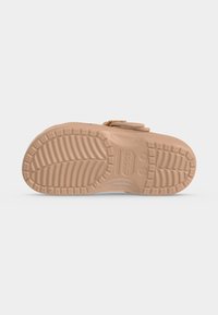 Μπεζ λαστιχένια σόλα σανδαλιού Crocs με βαθιά πέλματα και ενδείξεις μεγέθους σε απλό ανοιχτό γκρι φόντο.