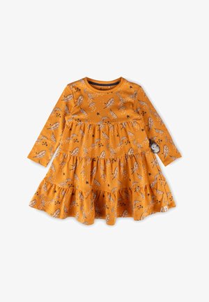 Langärmliges Kleid in Senfgelb, mit geschichteten Rüschen, die ein Blatt- und Sternmuster zeigen, und einem kleinen dekorativen Patch am Ärmel.