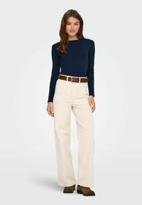 Granatowa bluzka z długim rękawem zestawiona z kremowymi, szerokimi spodniami i brązowym paskiem. Stylizację dopełniają brązowe botki za kostkę. Prosty i nowoczesny design.