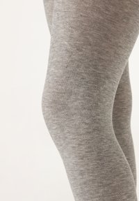 Grå leggings tillverkade av ett mjukt, elastiskt tyg, med en slät yta och figurnära design, som visar en närbild av tygets yta.
