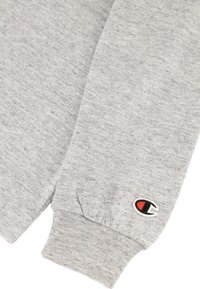 Grauer Sweatshirt mit geripptem Bündchen, weichem Material und kleinem gesticktem Logo in Rot, Schwarz und Weiß auf dem Ärmel.