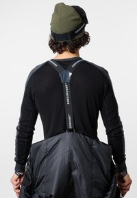 Mustapaita, jossa on pitkät hihat ja harmaita yksityiskohtia, sisältäen kamotaukun ja mustan toppatakin, jota pitää yllä henkilö, jolla on oliivinvihreä pipot.