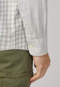 Camisa a cuadros en gris claro y blanco con puños abotonados y una ligera textura, combinada con pantalones cargo en verde oliva.