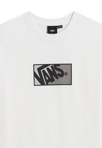 Bílý bavlněný tričko s velkým černým obdélníkovým logem, na kterém je uprostřed hrudi text "VANS" tučným písmem. Krátký rukáv.