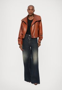Chaqueta de cuero marrón corta con cuello ancho, combinada con unos vaqueros de mezclilla oscuros de tiro alto y pernera acampanada que presentan un ligero desgaste.