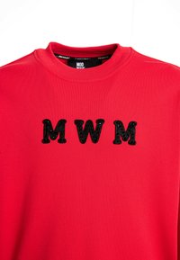 Sudadera roja con cuello redondo que presenta tres letras negras bordadas "MWM" en el frente. Material suave con una textura lisa.