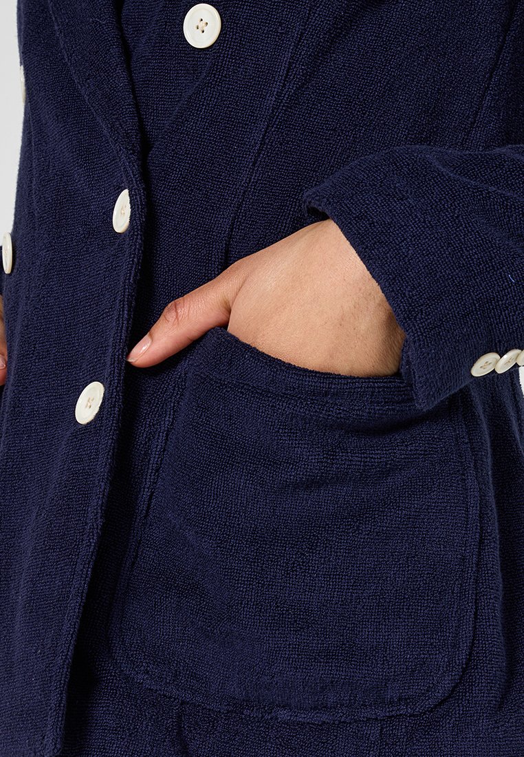 Granatowa teksturowana kurtka z kieszenią, dużymi białymi guzikami i dopasowanym krojem z wyciętym kołnierzem.