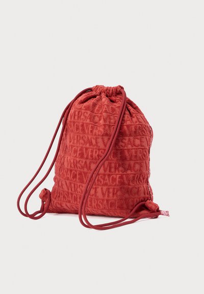 Κόκκινη τσάντα με κορδόνι από βελούδο με ανάγλυφα λογότυπα "Versace", στρογγυλεμένο σχήμα και κορδόνια σε αντίθετο χρώμα. Συμπαγής και ελαφρύς σχεδιασμός.