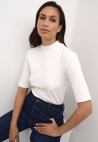 Top alb cu mâneci scurte, cu dungi, și gât înalt, asortat cu blugi din denim închis cu talie înaltă, buzunare frontale și finisaj albastru.