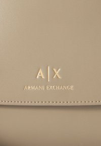 Beige leather surface with gold embossed "A|X Armani Exchange" logo and visible stitching detail.