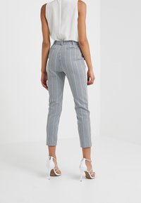 Pantaloni a quadri blu e bianchi, adatti e con vita alta, a gamba affusolata. Abbinati a sandali con tacco alto e bretelle bianchi.