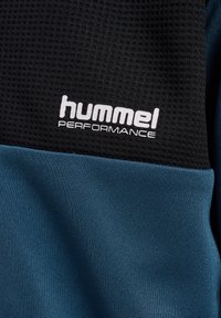 Zwart en blauw sportstof met een gestructureerde oppervlakte. Bevat het "hummel PERFORMANCE" logo in het wit. Glad blauw gedeelte met fijne ribbels.