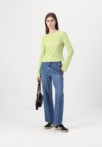 Lys grønn ribbet langermet topp, sammen med høyhalset blå denimjeans. Skoene har svart med hvite striper. Svart håndveske.