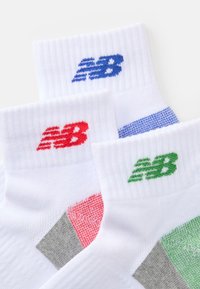 Meias de tornozelo brancas com detalhes coloridos em vermelho, azul e verde. Apresentam uma bainha canelada e o logo "NB" bordado. Textura de tecido durável.