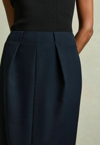 Gonna di un blu navy scuro con pieghe laterali, texture liscia e vestibilità su misura. La vita è pulita e si adatta comodamente al corpo.