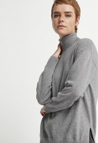 Ljusgrå polotröja med ribbad krage och mudd, med sidofickor. Mjuk textur, avslappnad passform och minimalistisk design.