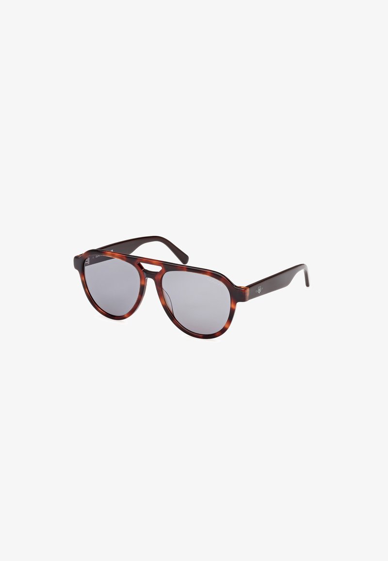 Gafas de sol de carey con lentes redondeados y tinte gris. Están hechas de plástico con brazos delgados oscuros, y cuentan con acentos de logo en los laterales.