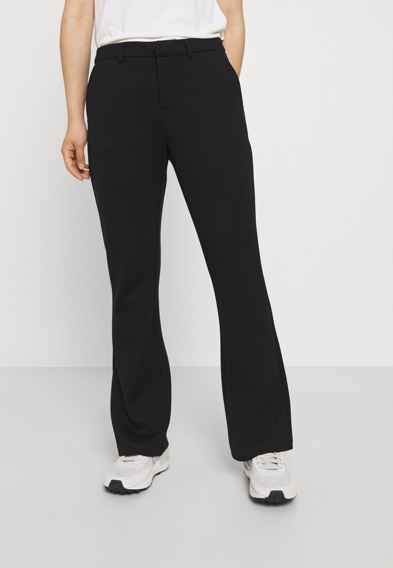 Black flared pants made from a smooth fabric, featuring a flat front and concealed zipper. Worn with white athletic shoes.