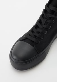Mustad mustad sneaker musta kangaga, millel on kangast ülemine osa, kummist varbakatte ja tekstuuriga kummist tallad. Nöörid, mis on läbi viidud viiest silmade paarist.