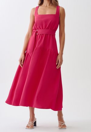 Mujer con un vestido midi sin mangas de color rosa brillante, escote cuadrado, cinturón ancho y sandalias blancas con tacón.