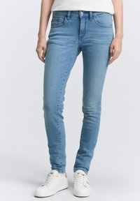 Světle modré džíny skinny s středním pasem, tradičním pětipocketovým designem a jemnými detaily odrůžovění. Doplnené bílými teniskami.