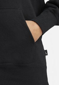 Felpa nera con tasca a marsupio, polsini a costine e una piccola etichetta con logo. Tessuto morbido e testurizzato con una vestibilità standard.