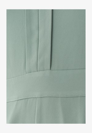 Jasnozielony materiał o gładkiej fakturze, z pionowymi szwami i poziomą linią ściegów, wskazującymi na dopasowany fason.