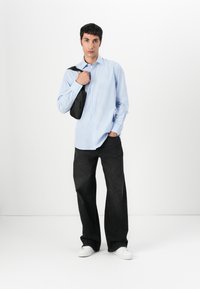 Blå og hvit stripet skjorte med knapper, løstsittende mørkeblå jeans og hvite joggesko; bærende en liten svart skulderveske.