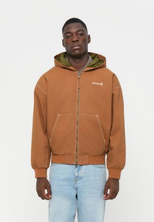 Brown zip-up hoodie with a green inner lining, featuring large front pockets and ribbed cuffs. Timberland logo displayed on the chest.
