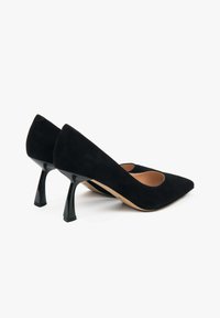 Czarne zamszowe szpilki z ostrym noskiem i otwartym cięciem, z czarną błyszczącą szpilką o unikalnym kształcie. Gładka, wewnętrzna podszewka, minimalistyczny design.
