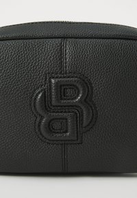 Black textured leather cosmetic bag with embossed logo, zip closure, and subtle stitching details. Compact, rectangular shape.