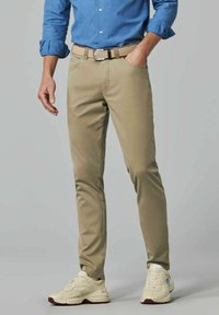 Beige broek in een slim fit, gemaakt van duurzaam materiaal. Heeft een gevlochten riem en is gecombineerd met lichtgekleurde sneakers.