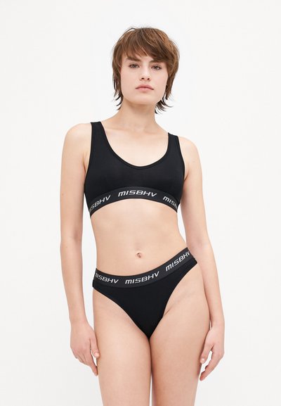 Black bralette and thong set made from smooth fabric. Bralette features a scoop neckline and a branded elastic band. Thong has a similar band.