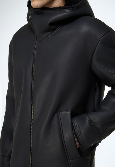 Schwarze Lederjacke mit hohem Kragen, ausgestattet mit einem Frontreißverschluss, Seitentaschen und weichem Fellfutter an Kapuze und Bündchen.