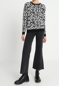 Zwarte trui met witte luipaardprint, geribde manchetten, gecombineerd met zwarte flared jeans en chunky zwarte veterschoenen.