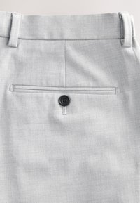 Pantalon habillé gris clair avec poche arrière fermée par un bouton noir et passants de ceinture à la taille.