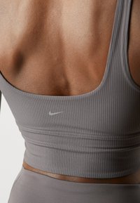 Sivkasta rebrasta športna široka srajca z rahlim logotipom Nike. Teksturna tkanina s prilegajočim se dizajnom poudarja telo.