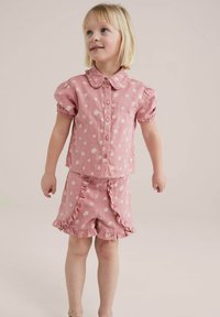 Camisa corta de manga con flores rosas y un cuello rizado, acompañada de pantalones cortos a juego. Ambos tienen un patrón de flores blancas y bordes rizados.