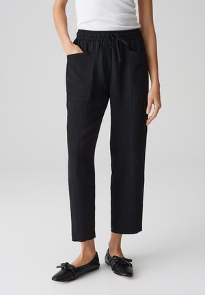 Pantalons noirs à coupe ample avec une taille élastique et un cordon de serrage. Dotés de deux poches avant et d'une texture lisse. Stylés avec des ballerines noires.