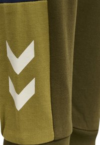 Gröna träningbyxor med strukturtyg, lagerdesign med mörkblå accenter och vita chevronmönster på sidan.