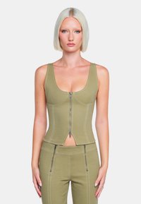 Olivgrünes, tailliertes Tanktop mit einem Reißverschluss vorne, das kontrastierende weiße Nähte und ein Ausschnittdetail am Saum aufweist.