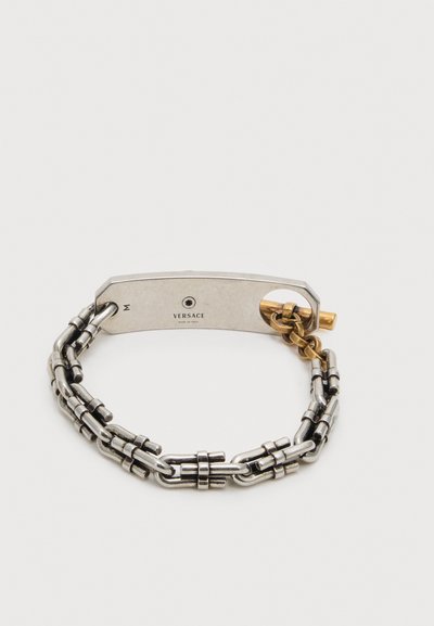 Διπλό ασημένιο βραχιόλι με ασημένια ορθογώνια πλάκα χαραγμένη με "Versace Made in Italy" και μικρό χρυσό κούμπωμα.