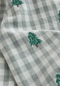 Tissu à carreaux gris et blanc avec des arbres brodés en vert, présentant une texture douce et une apparence superposée.