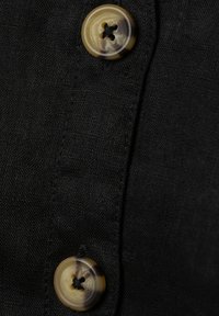 Zwarte stofdetail met twee ronde, gemarmerde knopen met een viergatsontwerp, bevestigd langs de rand van het kledingstuk.