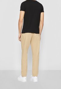 T-shirt noir à manches courtes associé à un pantalon beige et des baskets blanches. La tenue présente un design simple et décontracté avec une coupe relaxe.